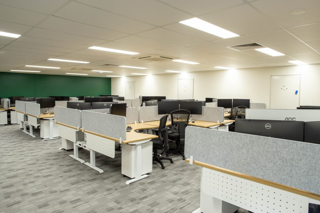 A wide-angle shot of a room with workstations and a dark green feature wall.