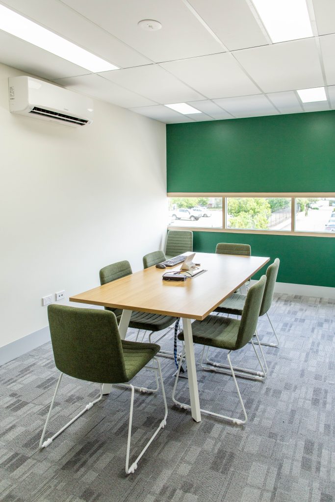 A portrait shot of an office meeting room with green chairs and a window